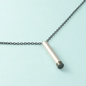Close-up of a silver stainless steel cylindrical pendant on a sleek black cord necklace
