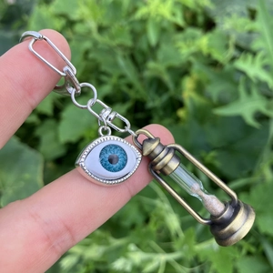 Detailed close-up of a bronze hourglass and blue eye pendant on a metal keychain