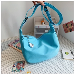 Detail of sky blue crossbody dumpling bag with fabric texture and white puppy charm