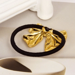Detail of high-quality black elastic hair tie featuring a polished gold metallic bow charm