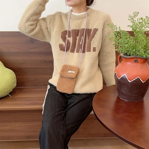 Detail of plush brown phone bag with purple strap shown in a cozy lifestyle setting