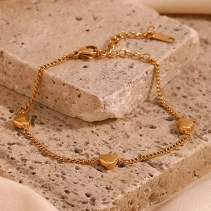 Detailed view of an 18K gold plated stainless steel heart charm bracelet on a stone surface