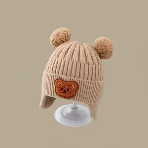 Detail of warm knit baby hat featuring plush bear patch and cute double pom-poms