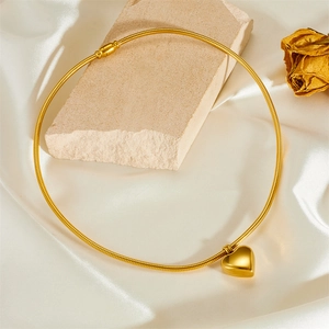 Close-up of golden heart pendant on snake chain over stone and silk background