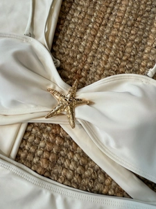 Détail d'un haut de bikini blanc avec une boucle étoile de mer dorée sur tissu texturé