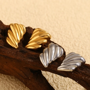Macro view of textured wing earrings in gold and silver plating on wood background