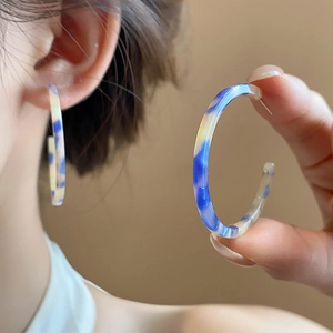 Detailed view of large C-shaped resin earrings featuring blue marble texture and silver pins