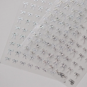 Detailed macro view of silver bow nail art stickers with small rhinestones on film