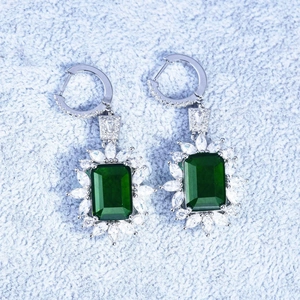 Close-up of emerald-cut green gemstone earrings with white marquise halo setting