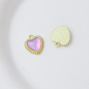 Macro detail of heart charm with pink stone, beaded gold edge and textured back