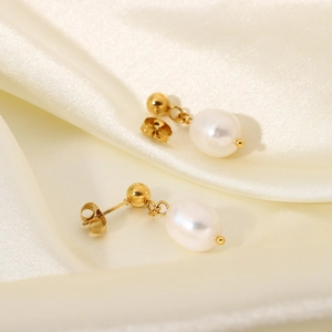 Macro view of freshwater pearl drop earrings with elegant golden studs on cream silk fabric