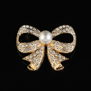 Broche nœud dorée élégante avec cristaux scintillants et perle blanche sur fond noir