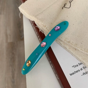 Detailed view of irregular teal acrylic hair clip with colorful inlaid rhinestones