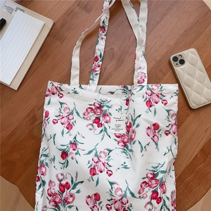 Detail of floral canvas tote bag with red tulip patterns on a rustic wooden desk