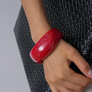 Close-up of a wide vibrant red acrylic bangle featuring a glossy semi-transparent finish