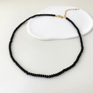 Elegant beaded necklace with black agate stones and gold clasp on white ceramic tray