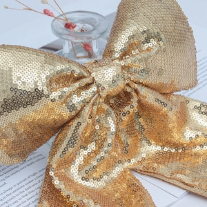 Large golden sequin bow ornament placed on glass bottle for Christmas decor