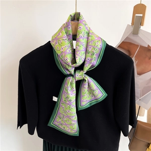 Détail d'un foulard étroit en soie à fleurs noué sur un pull en maille noir