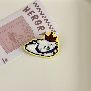 Detailed embroidery of a white cartoon cat patch with a red crown and blue scarf