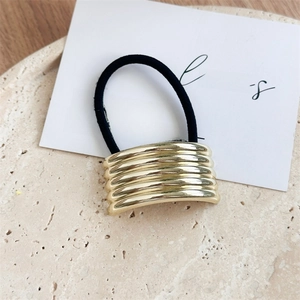 Close-up of golden wavy metal plate hair tie on a minimalist beige stone pedestal