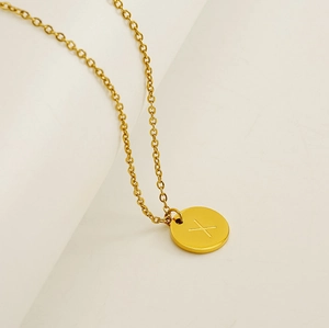 Gros plan d'un collier en acier inoxydable doré avec pendentif circulaire et lettre X