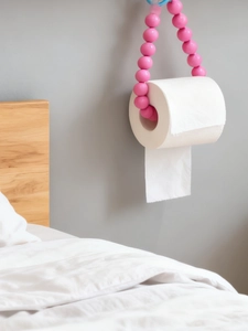 Detail of vibrant pink beaded toilet paper holder on a minimalist grey wall background