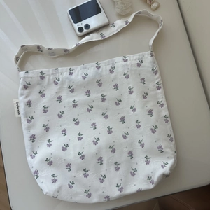 Close-up of white cotton shoulder bag with purple floral print and brand label