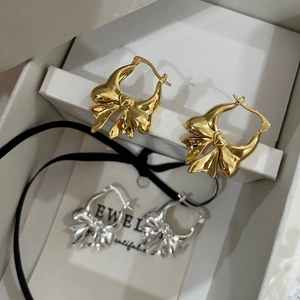 Macro detail of bow-shaped brass earrings in gold and silver finish inside a jewelry box