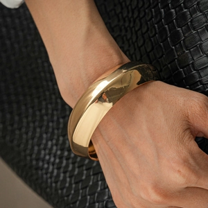 Close-up of wide golden geometric metal bangle with mirror finish on a person wrist