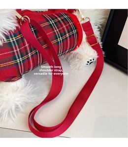 Close-up of red tartan cylinder bag with adjustable woven strap and gold metal hardware