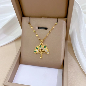 Golden Tree of Life necklace with green and white zircons in a beige jewelry box