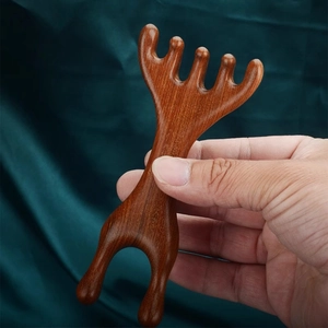 Detailed view of hand-held five-tooth sandalwood scalp massager on green silk fabric