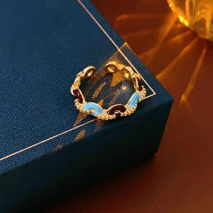 Dettaglio anello regolabile dorato con smalto blu e marrone e bordi con perline
