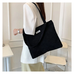Black corduroy tote bag shown on shoulder, featuring a minimalistic Fashion woven label