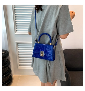 Detail of bright blue crocodile pattern handbag with golden metal lock and leather strap
