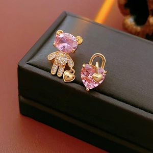Asymmetric gold bear and heart lock earrings with pink zircons on a jewelry box