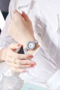 Close-up of a silver watch with a rhinestone bezel and shell dial on a woman's wrist