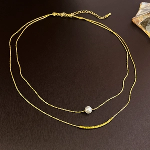 Double-layered gold necklace with faux pearl and geometric metal bar on brown background
