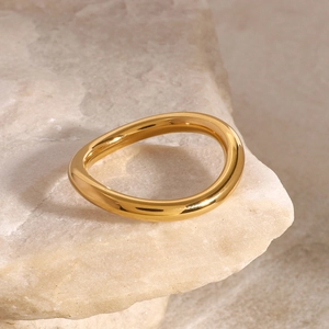 Macro shot of wavy gold polished ring resting on natural stone with soft lighting