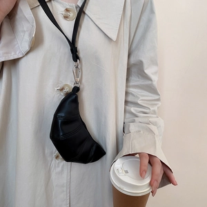 Détail d'une mini pochette croissant noire avec fermoir métallique sur un manteau