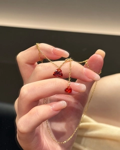 Macro detail of a golden necklace with two sparkling red heart pendants in hand