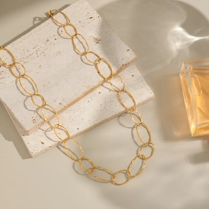 Golden oval chain necklace displayed on travertine stone with a perfume bottle