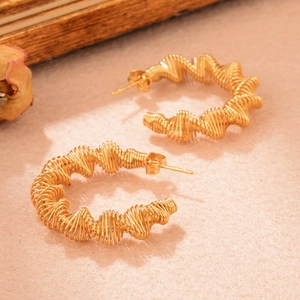 Macro détaillée de boucles d'oreilles en spirale dorée torsadée sur velours rose doux