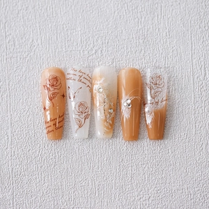 Amber and white press-on nails with rose patterns, pearls and crystal accents