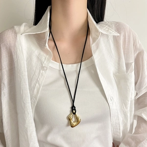 Close-up of a gold irregular geometric pendant on a minimalist black cord necklace