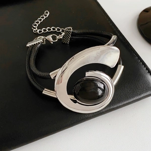 Detail of a black leather double-cord bracelet with an oval black stone in a silver pendant