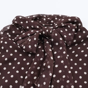 Detailed close-up of brown polka dot chiffon blouse with a decorative bow-tie neckline