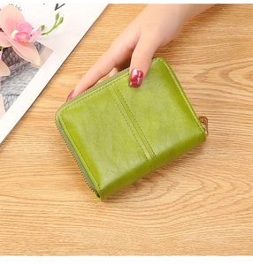 Close-up of a compact green leather zip-around wallet held in hand over a desk