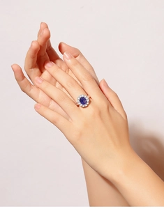 Close-up of an oval blue sapphire ring with clear gemstone halo worn by a model