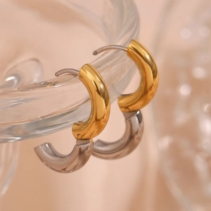 Close-up of minimalist gold and silver polished C-shape hoop earrings on glass